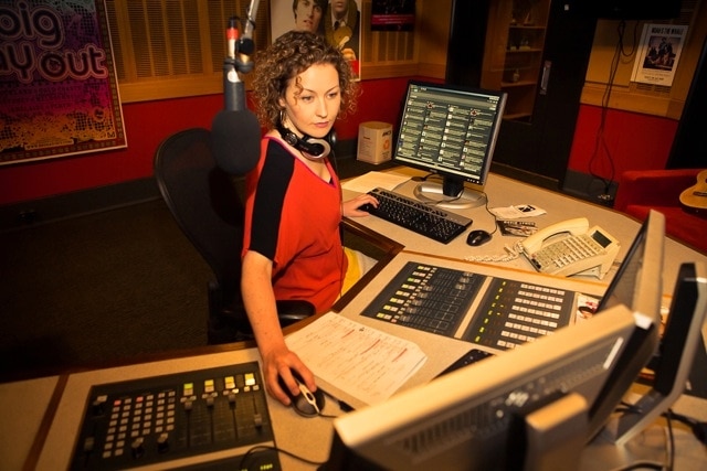 Woman in radio studio looking at mixing desk.