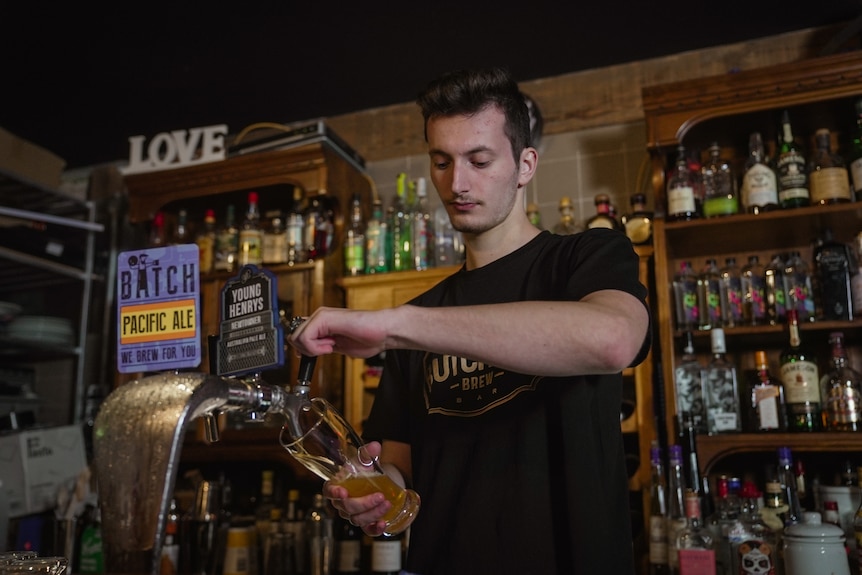 Luka Hackett pouring a beer at the music bar where he works.
