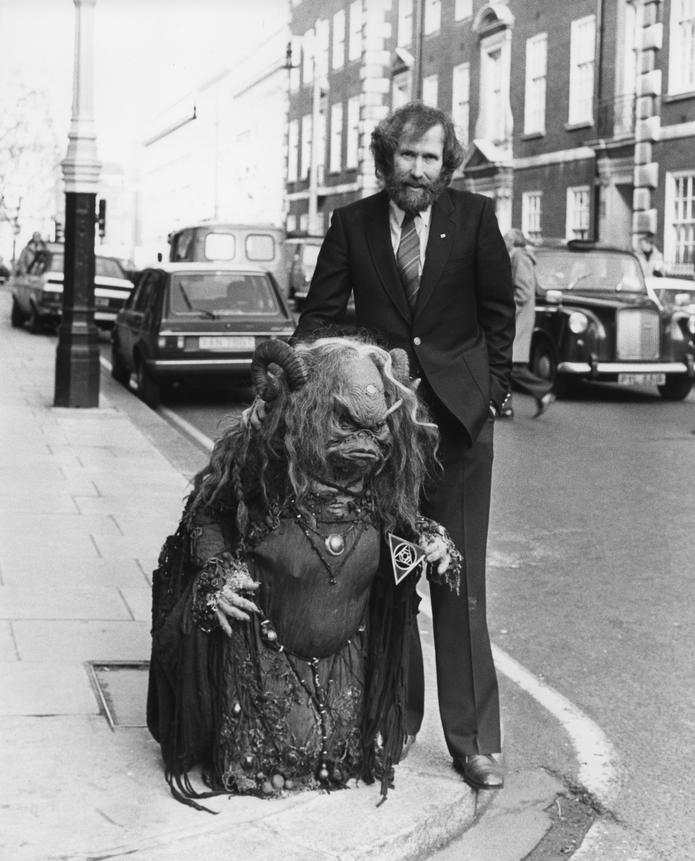 jim henson stands with a puppet on a street corner in suit and tie