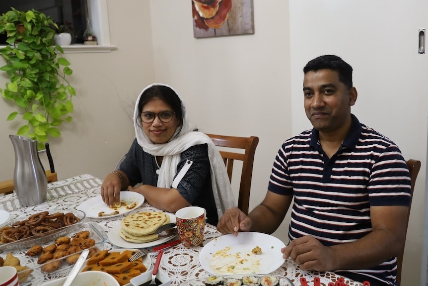 A woman and a man sitting at their dining table enjoying a meal with their family. 
