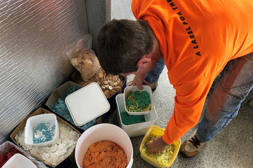 Recycler Brad Scott sorts through thousands of bread tags in boxes on the floor of his studio.