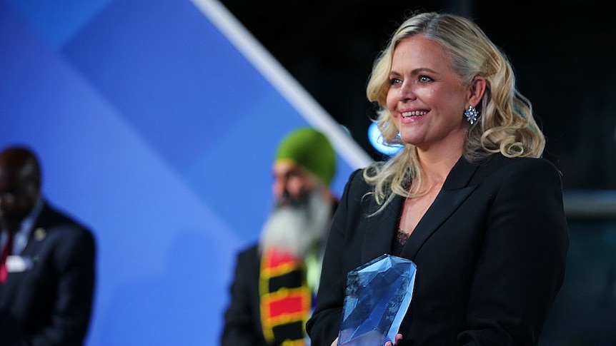 A woman holding an Australian of the Year award while smiling. 