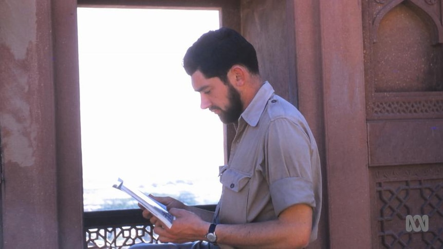 Man holds book beside wall