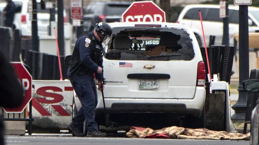 A Secret Service officer uses a mirror to check under a white passenger vehicle that struck a White House security barrier