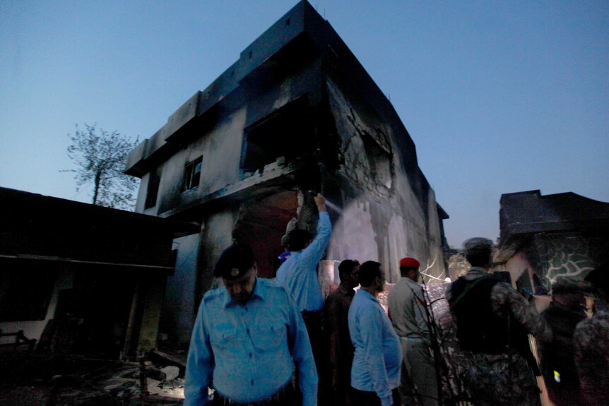 Army officers look around a badly damaged house