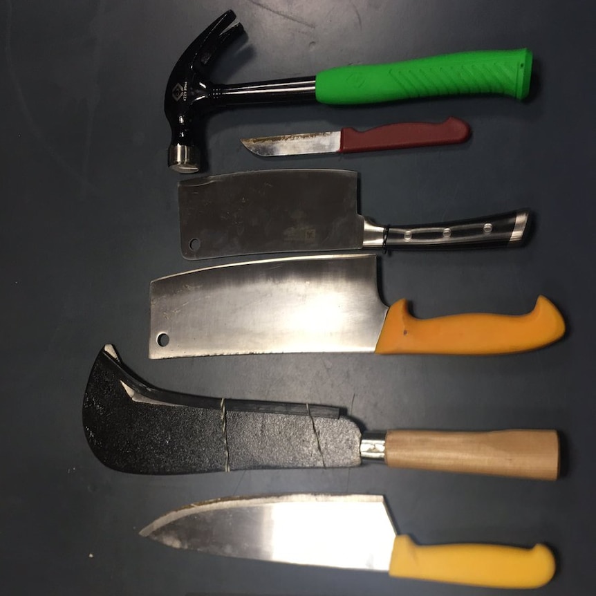 Kitchen knives, cleavers and a hammer are displayed next to a a ruler