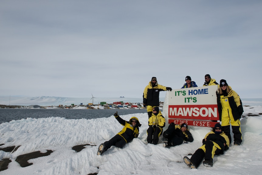 Expeditioners pose next to sign at Mawson Station.