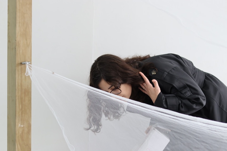 A young white woman with dark brown hair inspecting a white sheet 