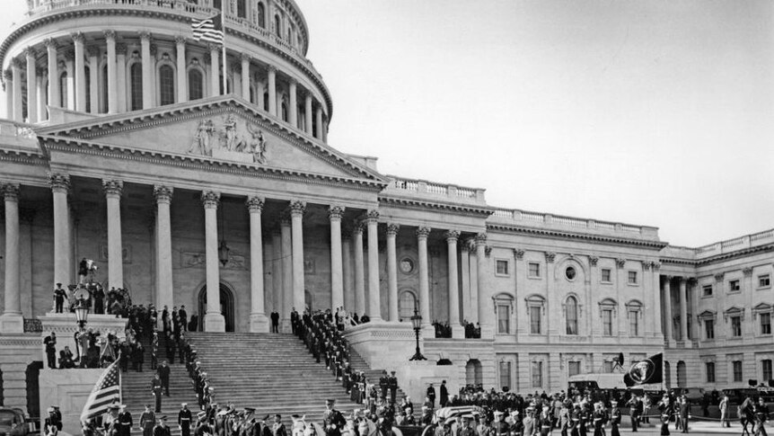 John F Kennedy's casket in front of Capitol Hill surrounded by people.
