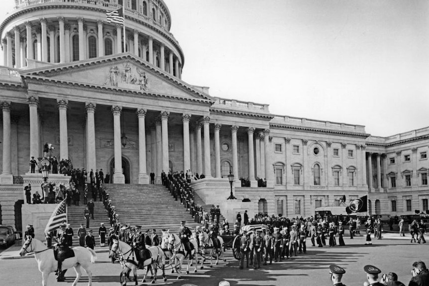 John F Kennedy's casket in front of Capitol Hill surrounded by people.