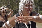 Two indigenous women in traditional dress practice their dance beside a river