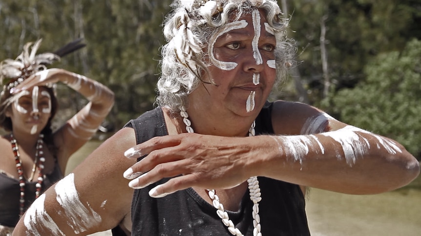 Two indigenous women in traditional dress practice their dance beside a river