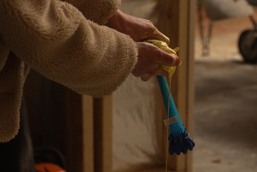 A person's hands hold a plastic tube with yellow paint spilling from it