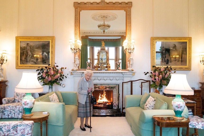 Queen Elizabeth in the drawing room with couches, tables, and lamps surrounding her