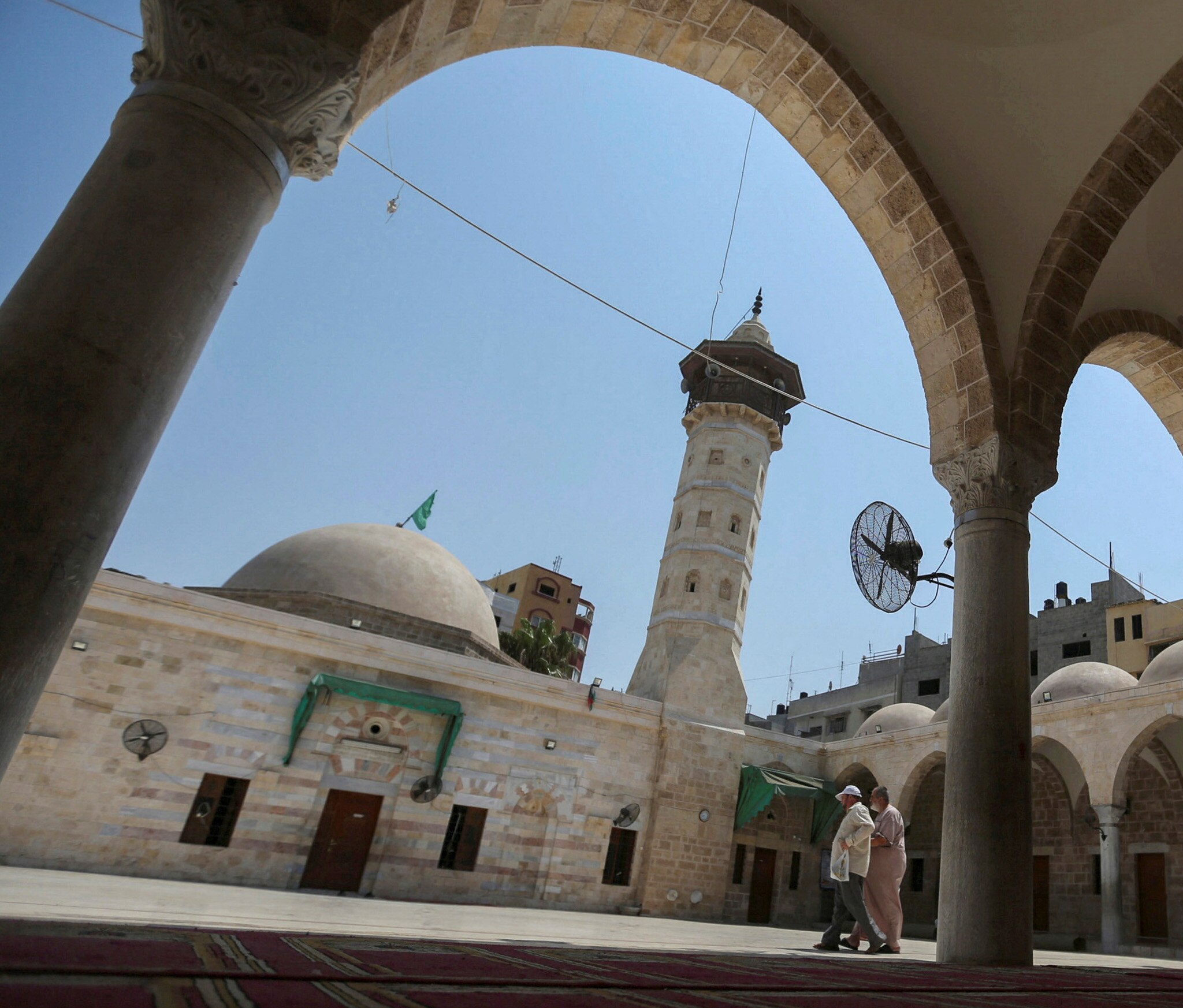 Palestinians walk by a mineret at a mosque.