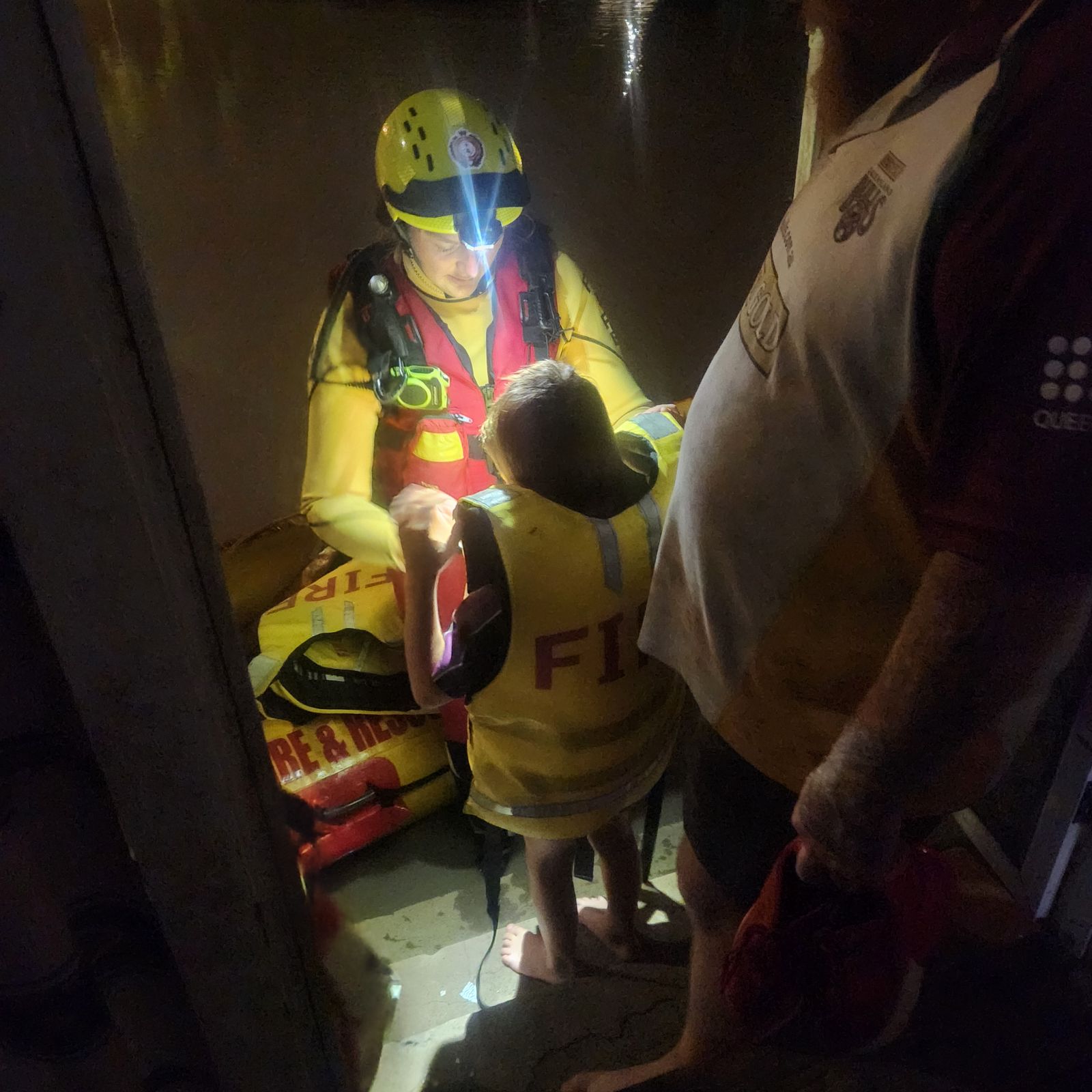 A child wearing a lifejacket standing in front of a swift water rescuer 