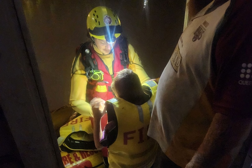 A child wearing a lifejacket standing in front of a swift water rescuer 