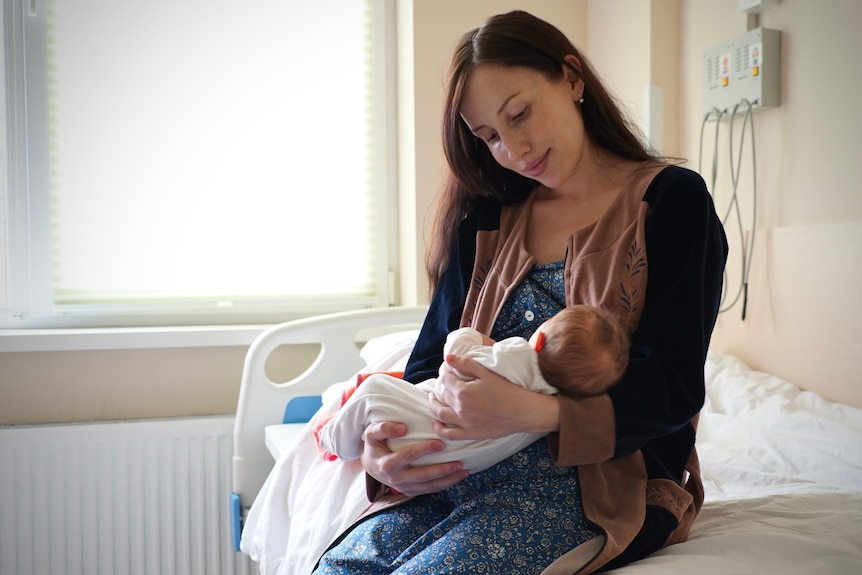 A new mother tenderly cradles her newborn child in a hospital room.