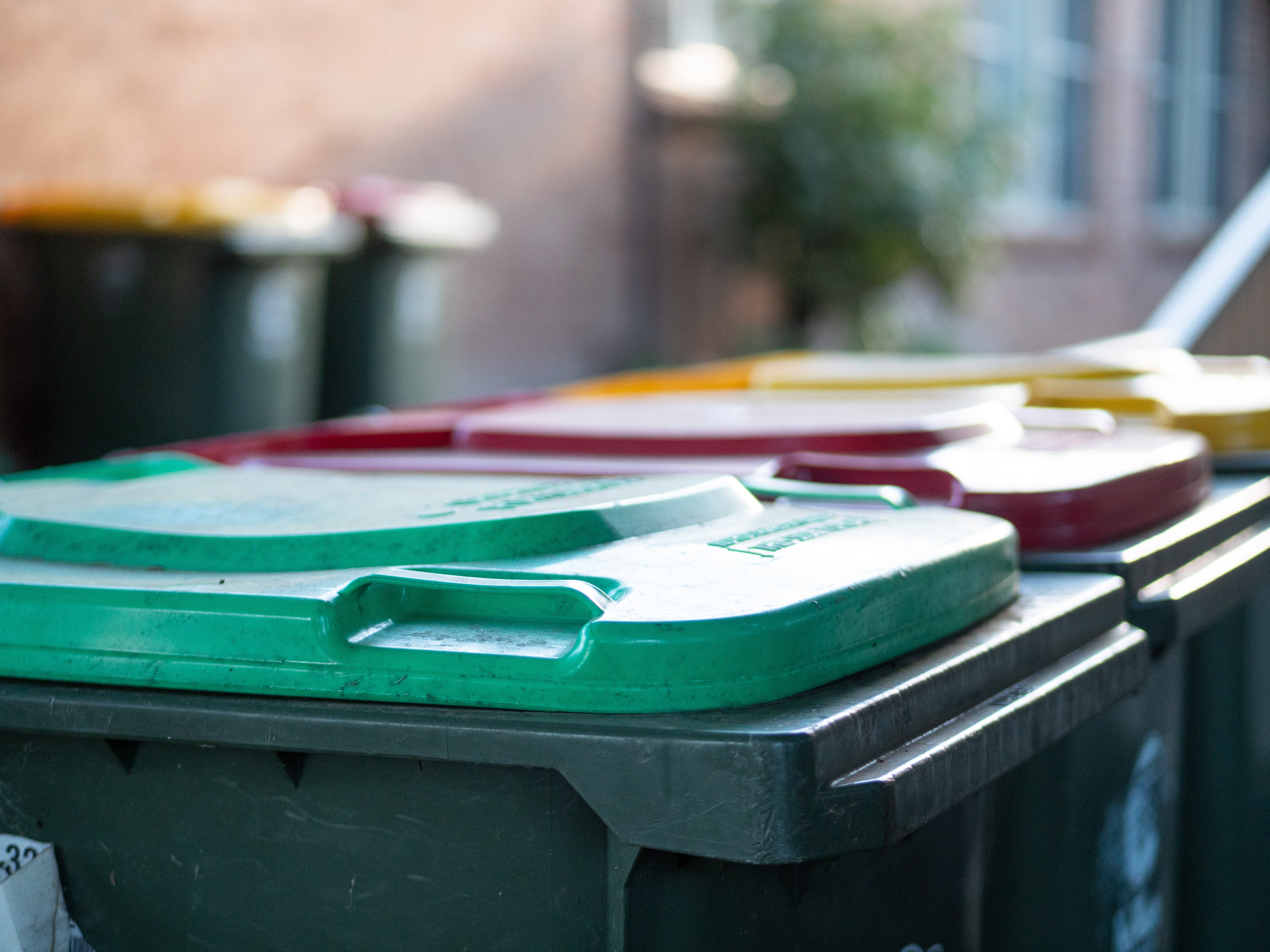 Contenedores comunitarios con tapas verdes en una calle suburbana.