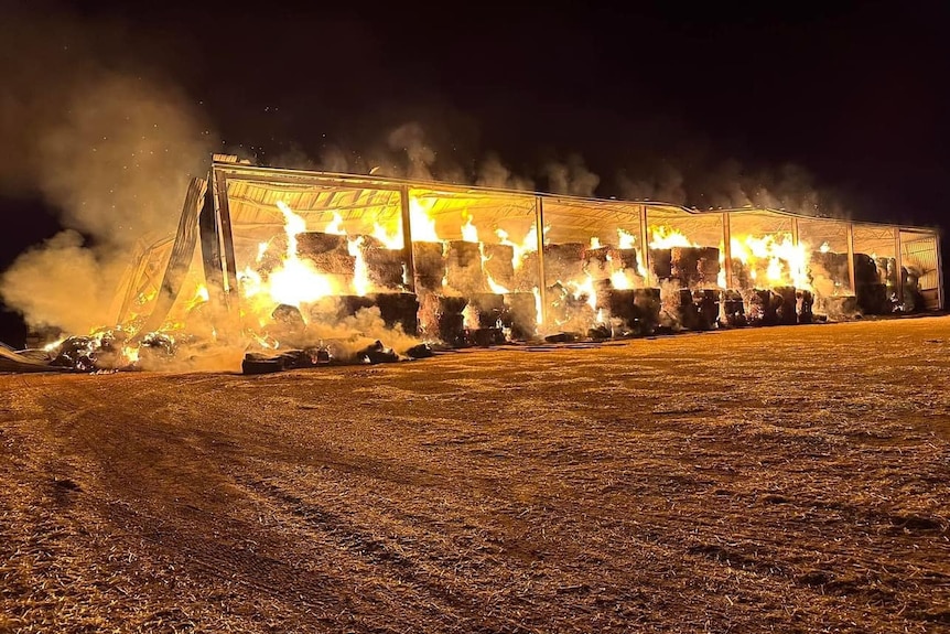 A shed filled with hay bales on fire at night.