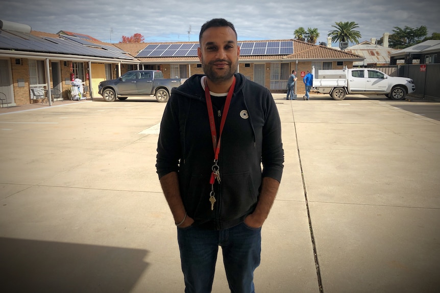 an Indian man stands in front of a block of motel rooms