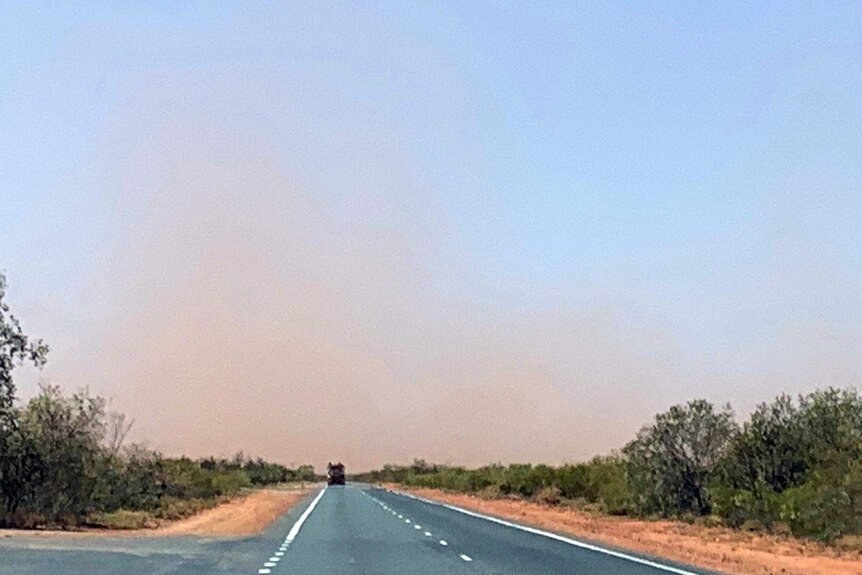 A photo of a highway with red dust in the air in the distance.