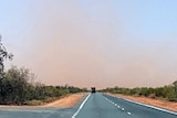 A photo of a highway with red dust in the air in the distance