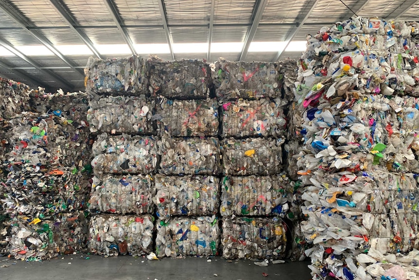 A picture of seven rows of recycling rubbing, stacked into squares and piled to a warehouse ceiling.