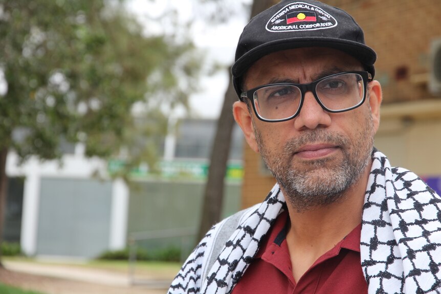 A man with a cap, glasses and wearing a keffiyeh stares past the camera