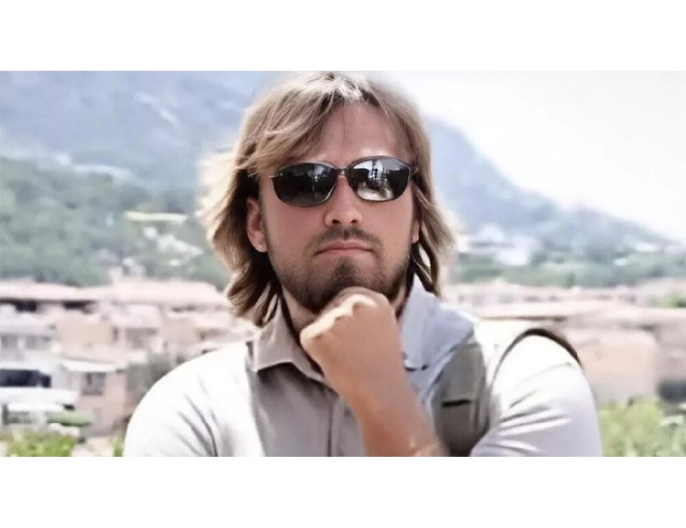 A man with a shaggy haircut rests his head on his chin 
