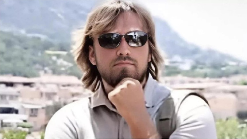 A man with a shaggy haircut rests his head on his chin 