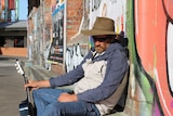 man slumped against graffiti wall, with sunglasses on, and guitar