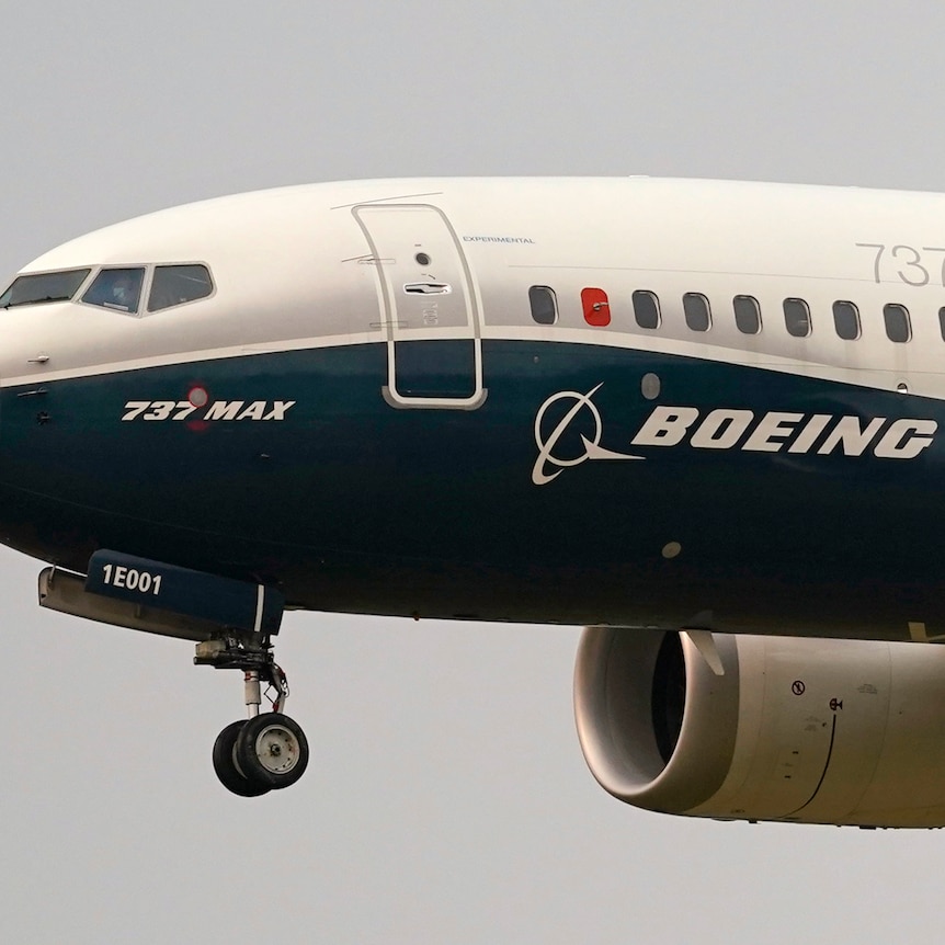 A close up of the front of a Boeing 737 MAX plane in the air, with its front wheels down