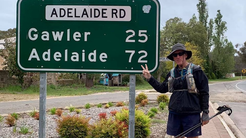 Man in walking gear standing in front of a road sign saying Adelaide