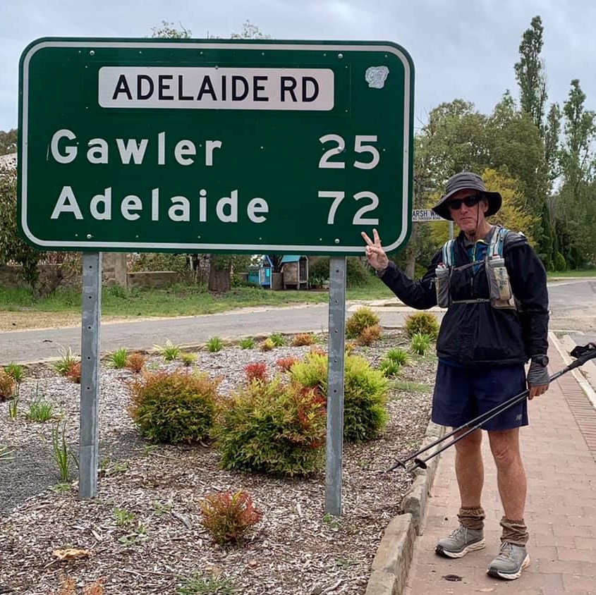 Man in walking gear standing in front of a road sign saying Adelaide