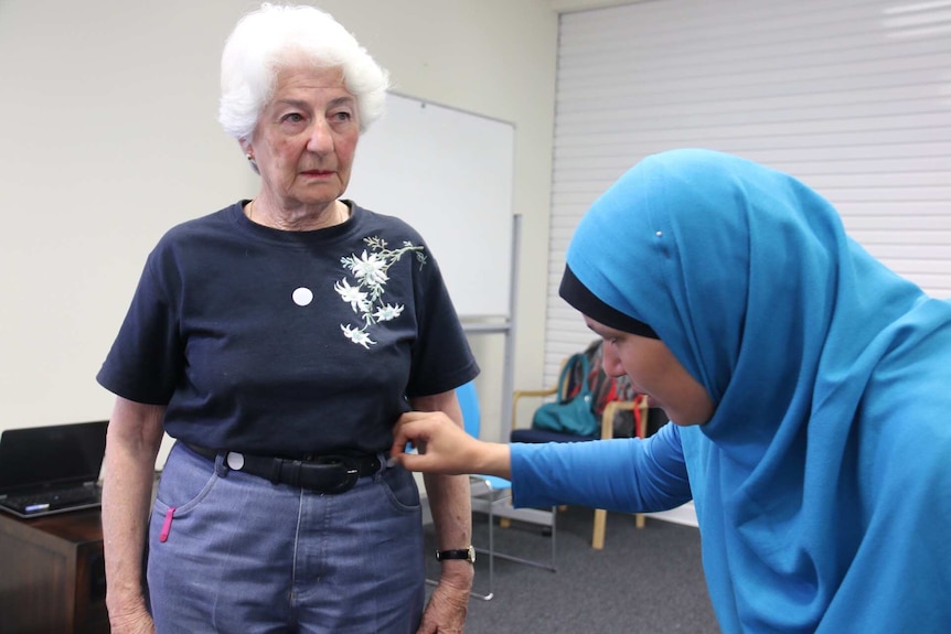A young woman places stickers in the chest and hips of an older woman.