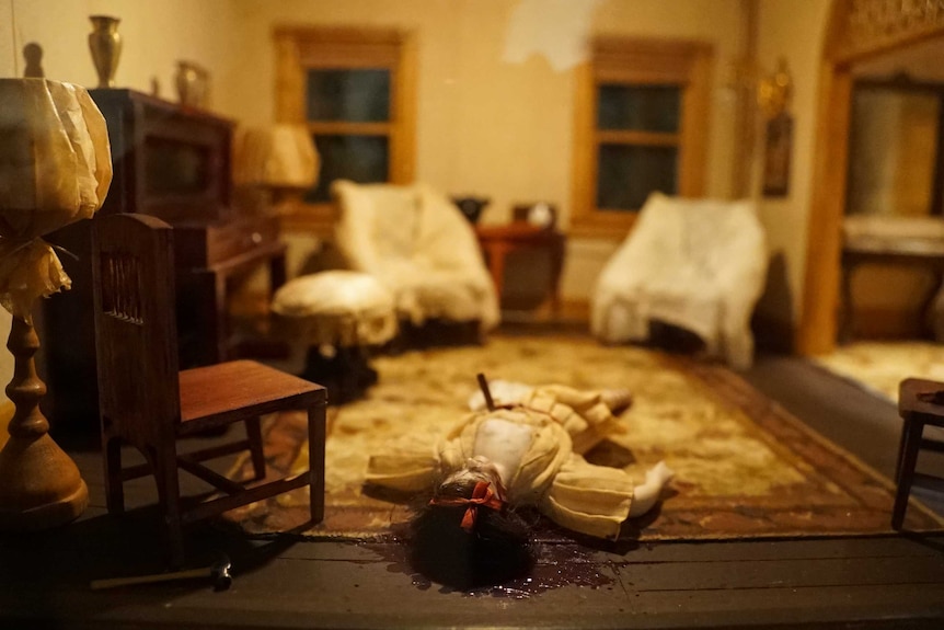 A tiny crime scene model - a woman on the floor of a parlour - stabbed, with blood beneath her head.