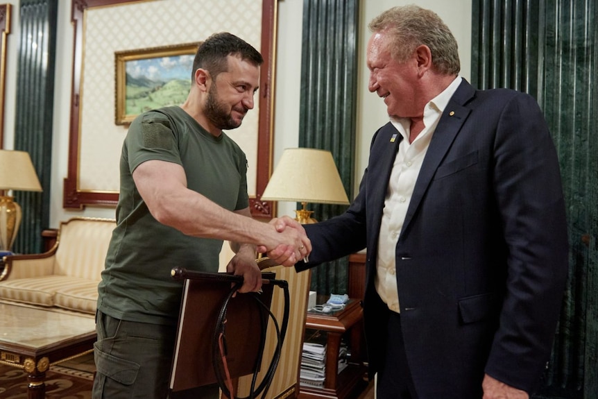 A man wearing green shakes the hand of a man wearing a suit. 