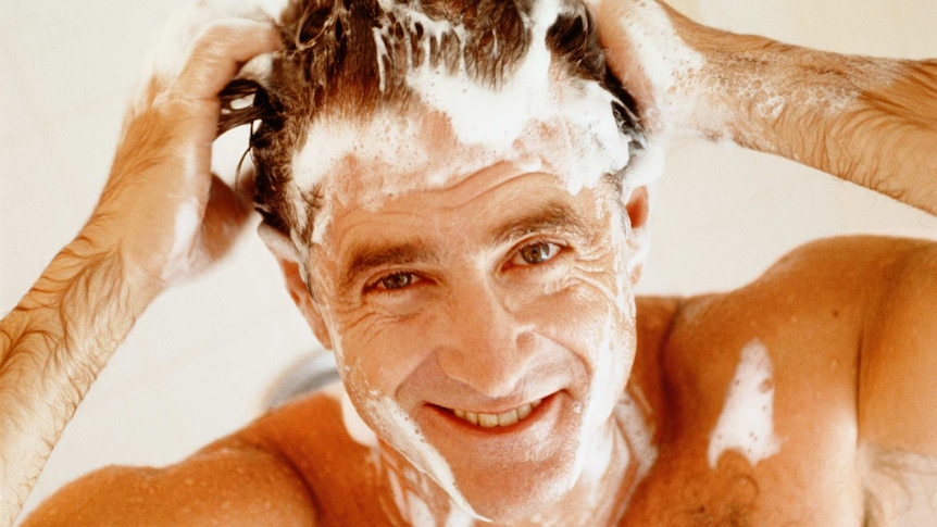 A man shampooing his hair smiling looking at the camera