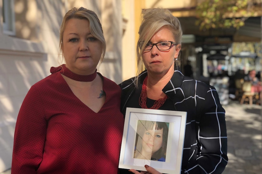 Michelle van Dyk and Sabine Kloss hold up a photo of Chrystal outside of court.