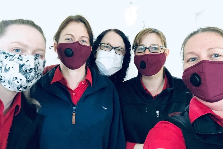 A selfie of five women in uniform wearing cloth face masks, white background.