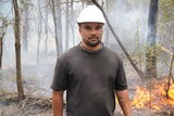 A man with a hard hat looks into the camera with controlled fire behind him.