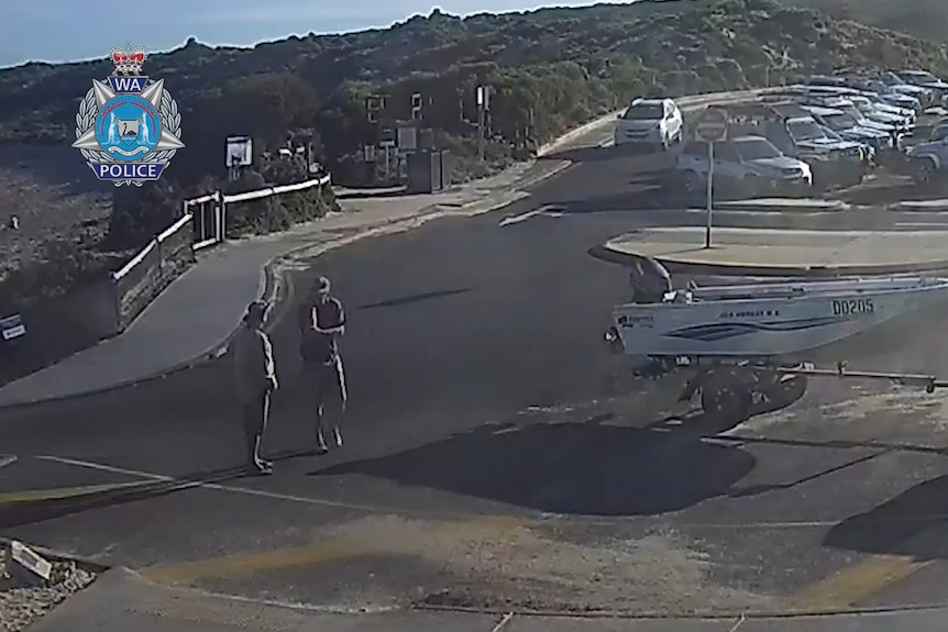 Two men speaking next to a boat trailer with a car park filled with cars in the background