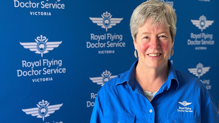 Cath walker stand in front of a royal flying doctor service background holding a medal