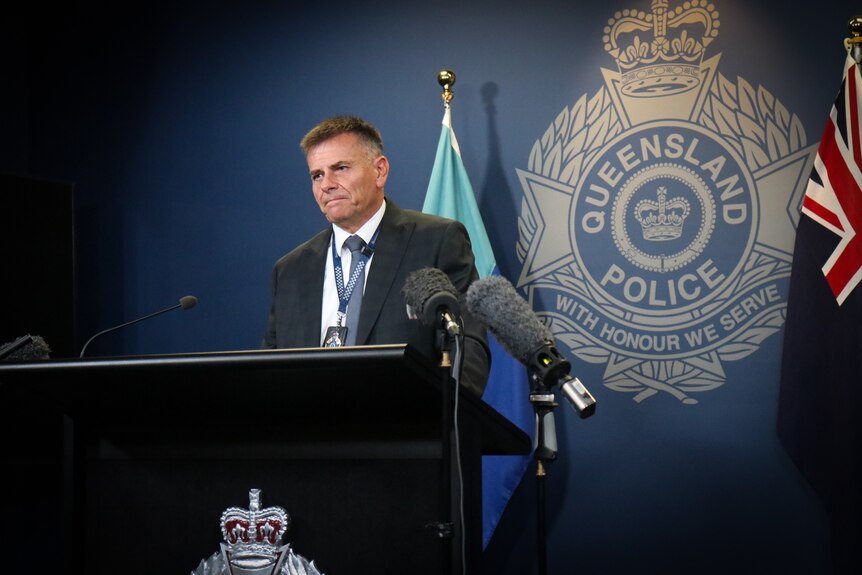 A policemen in a suit speaking at a podium in front of the police insignia. 