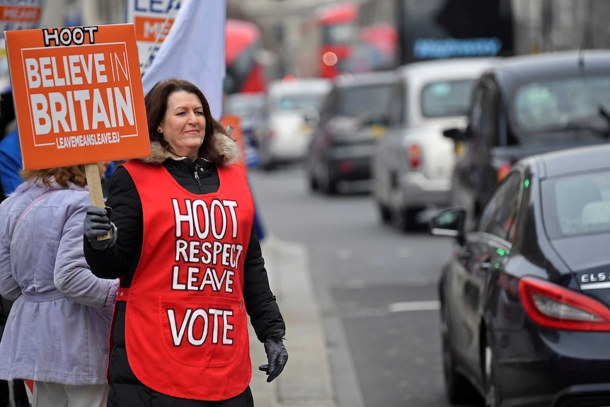 A woman attracts interest of passing cars with vest that says Hoot Respect Love Leave Vote