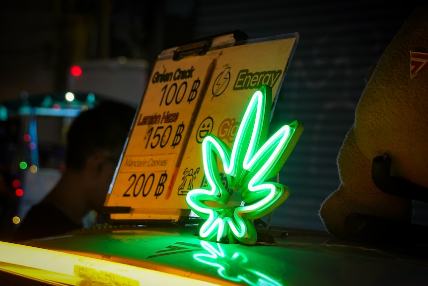 A neon cannabis leaf light next to a price list for various types of weed
