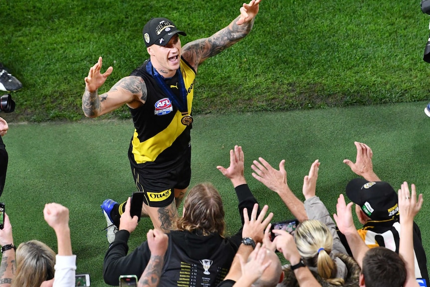 Dustin Martin smiles and raises his arms as he approaches the crowd, all of whom are reaching towards him