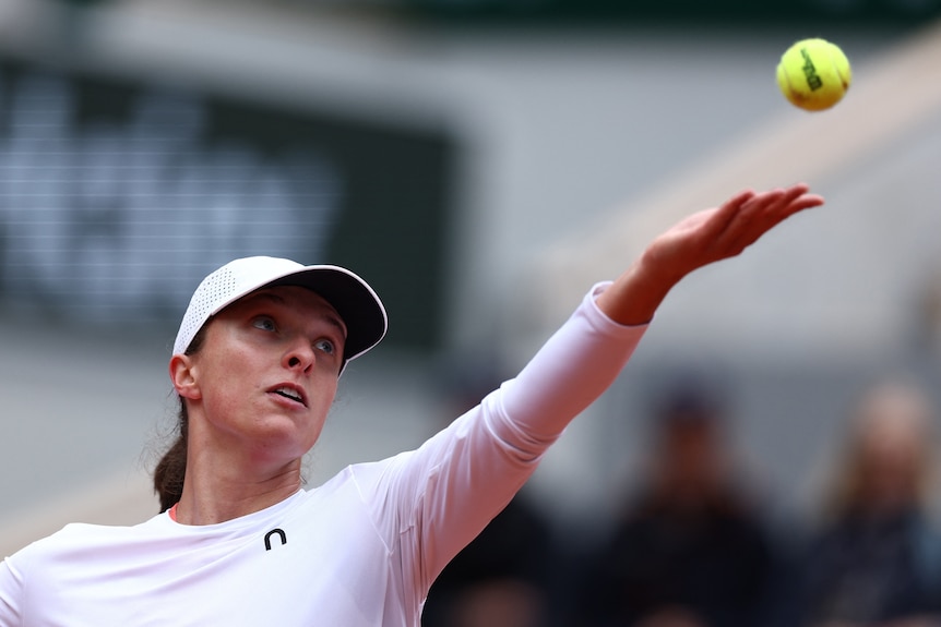 Poland's Iga Swiatek tosses a ball to serve during a French Open match, wearing white