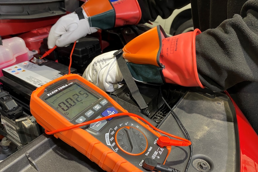 A man wearing gloves works on an EV.